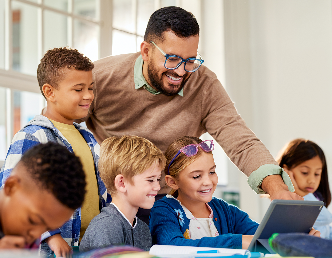 A teacher in a classroom showing three students how to do something on a tablet.
